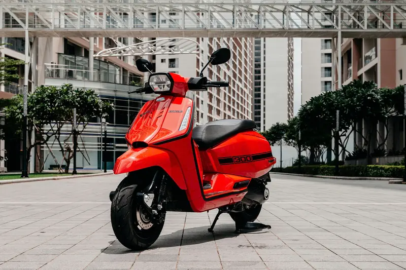 Lambretta X300 màu đỏ đậu trên sân lát đá giữa các toà nhà cao tầng